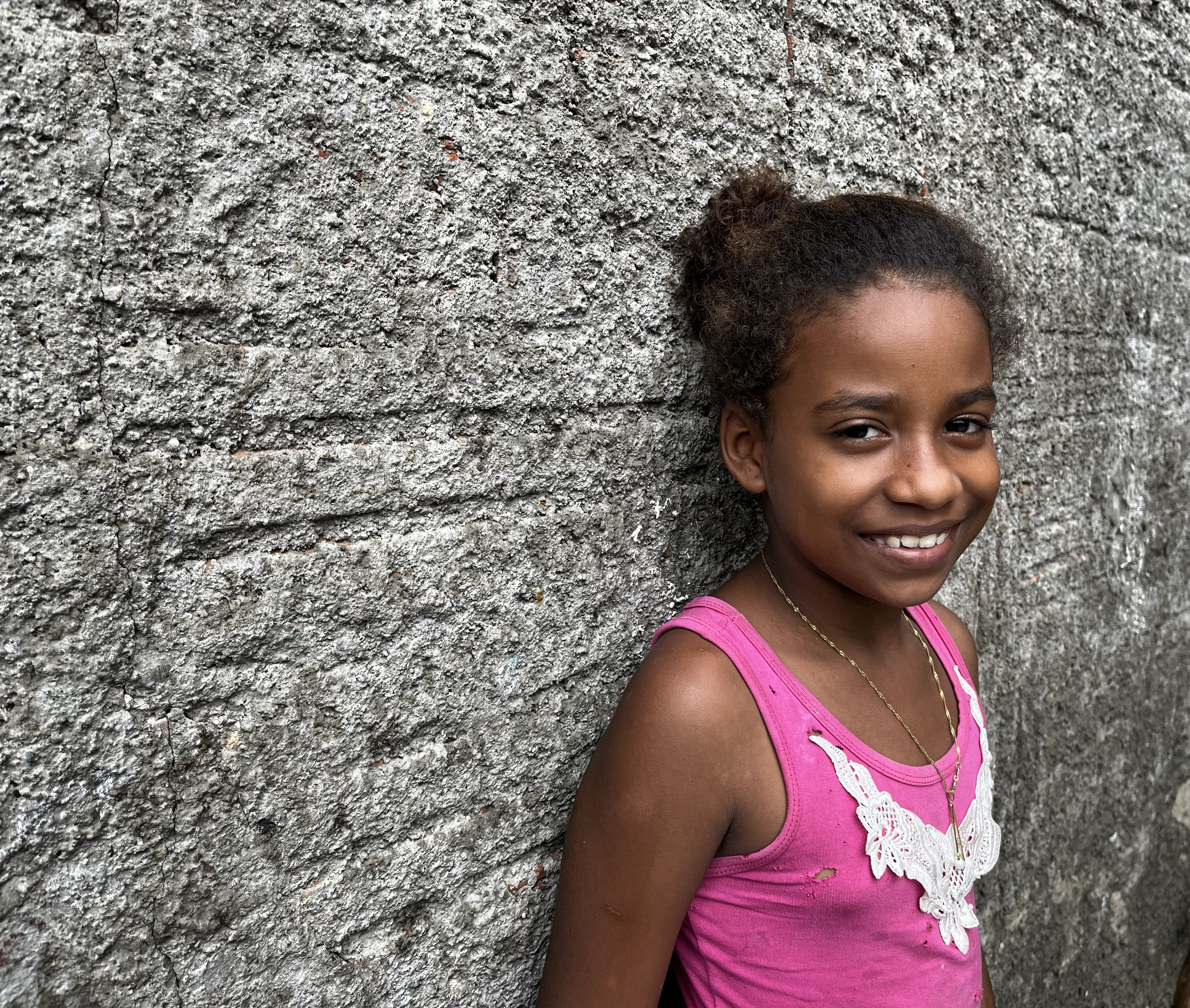 A girl dressed in pink is leaning against a grey wall, looking into the camera.